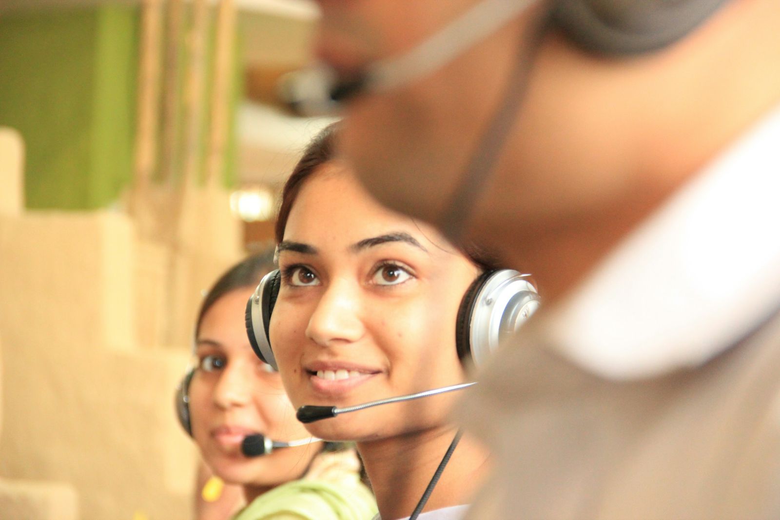 Two smiling women wearing headsets on calls in a bright office