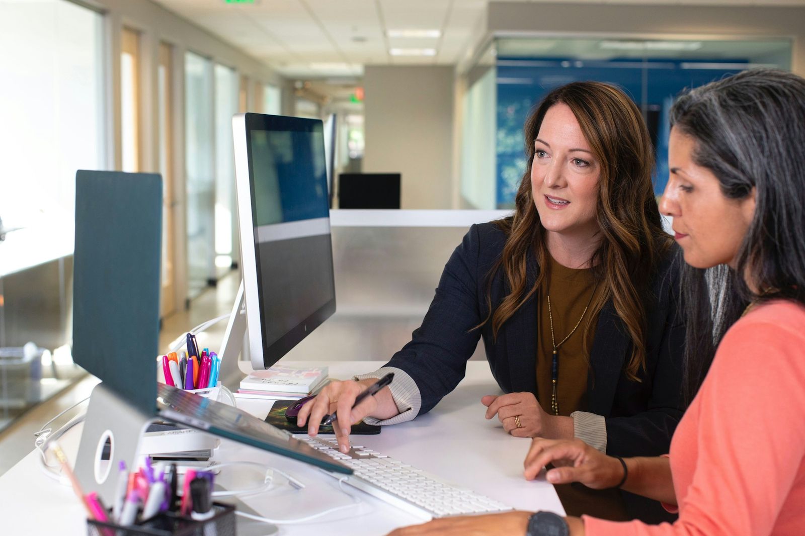 Two saleswomen discussing results at a desk with laptops in a bright office
