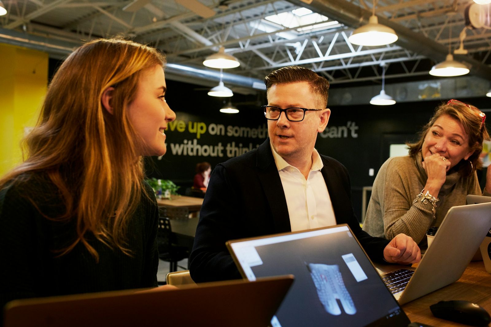 A sales team of three talking around laptops in a busy modern office